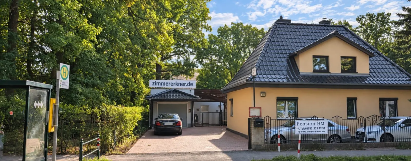 Casa de pe Neu Zittauer Straße 60 din Erkner, văzută din stradă: fațadă galbenă, carport cu locuri de parcare și stația de autobuz alături