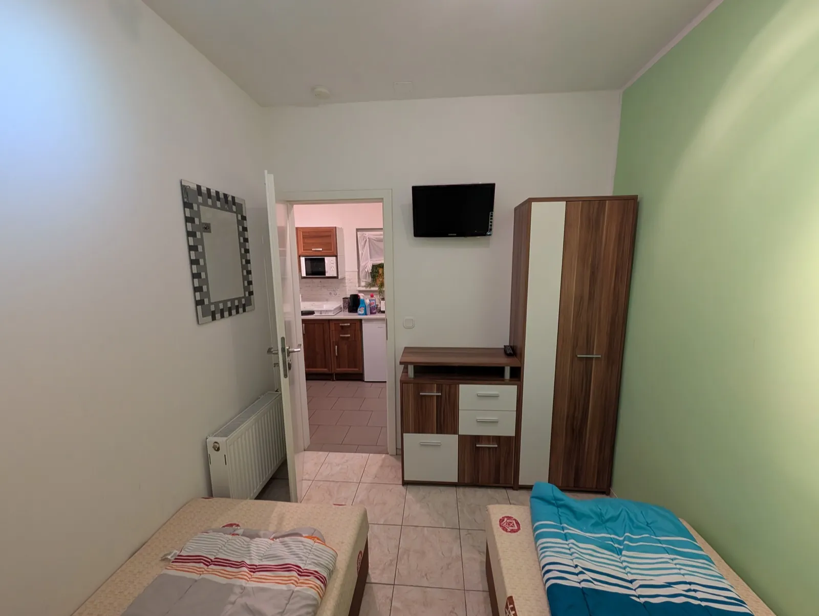 Erster Schlafraum der Wohnung Birke in Erkner mit zwei Einzelbetten, Fernseher und Kleiderschrank, dahinter der Durchgang zur Küche